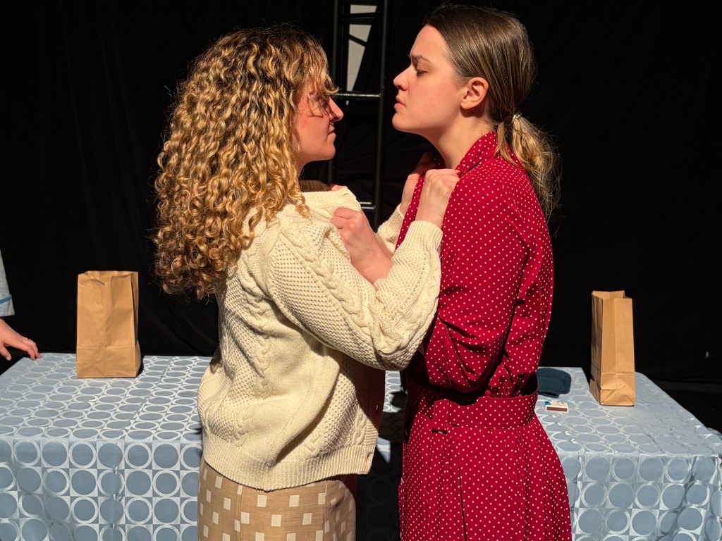 Two women, one in a beige sweater and one in a red polka dot dress, are grabbing each other's collars and are ready to fight.
